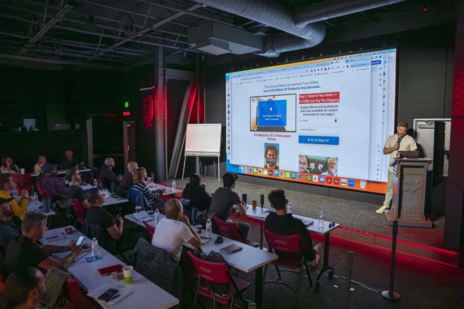 A packed room at the Pursuit of Profit Studio, presenter in front of the billboard screen